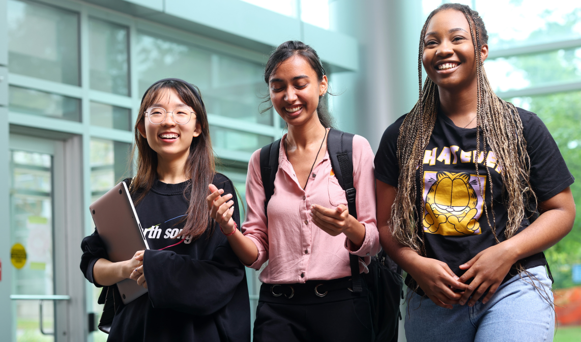 Three students chat as they walk through the lobby of the Rowe Management Building.